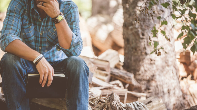 Man sitting on pile of chopped wood with a Bible in his hand