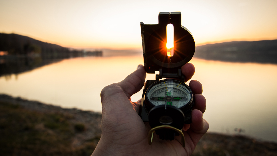 Man holding a compass looking at the sun