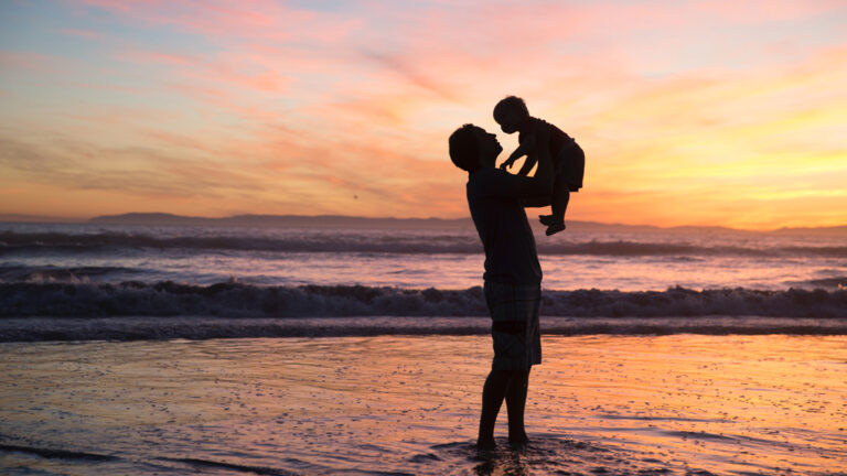 Man holding his son while standing in the ocean
