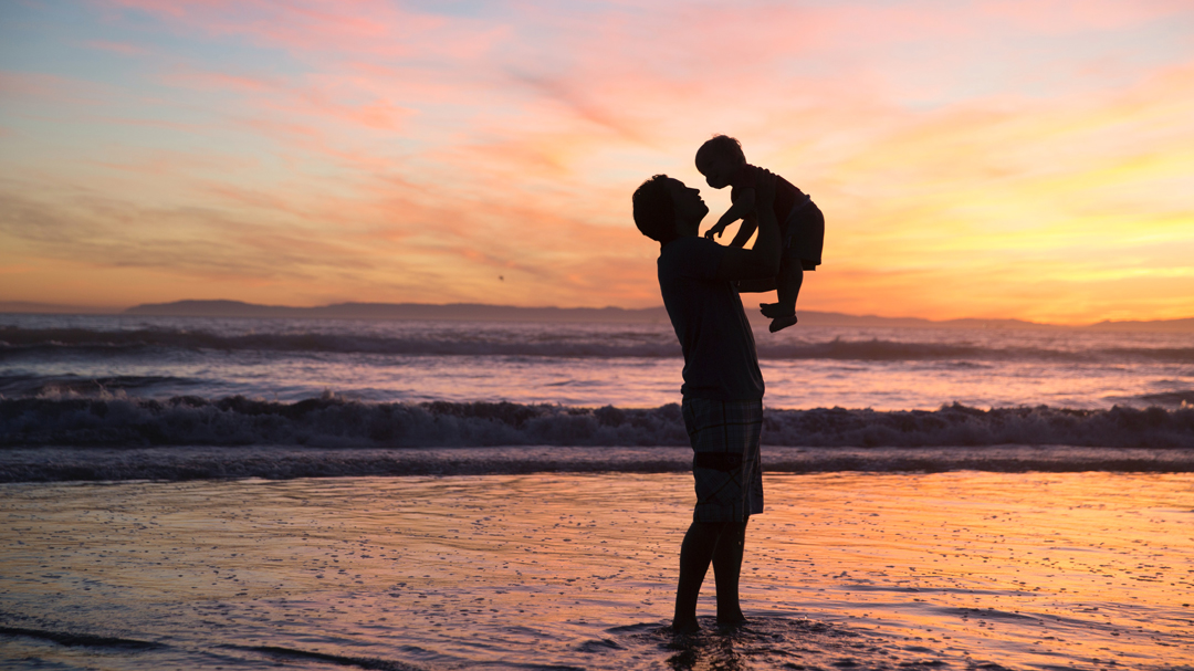 Man holding his son while standing in the ocean