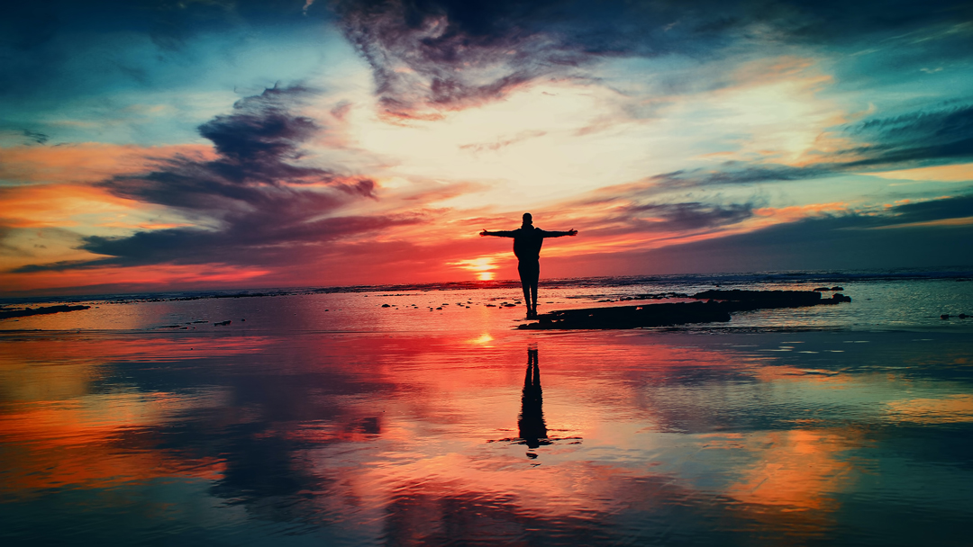 Person standing on rocks in the ocean looking at the sunset
