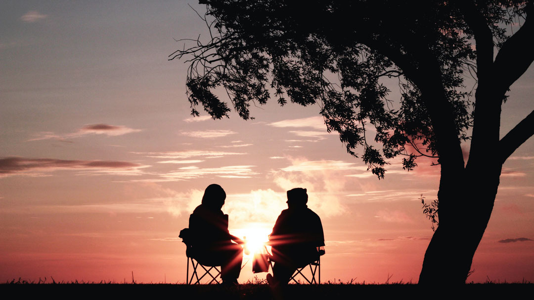 Two people sitting on camp chairs talking