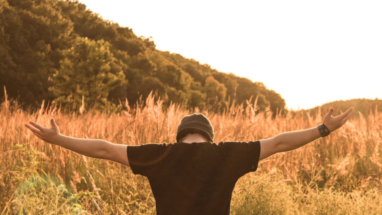 Man in grass field holding his arms out in praise