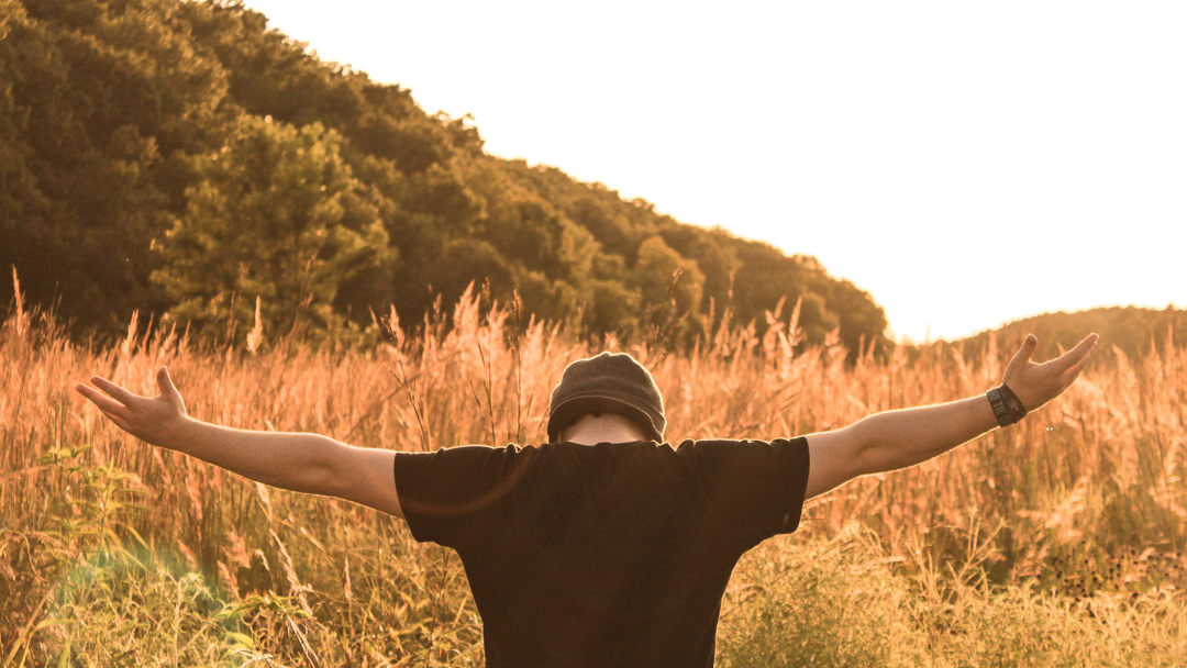 Man in grass field holding his arms out in praise