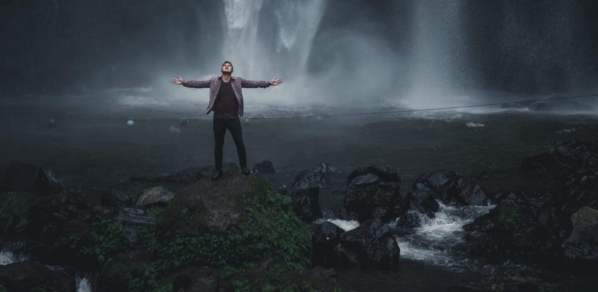 Man standing next to a waterfall with his arms out wide