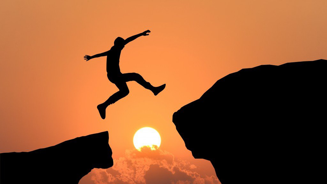 Silhouette of man jumping from one rock to another