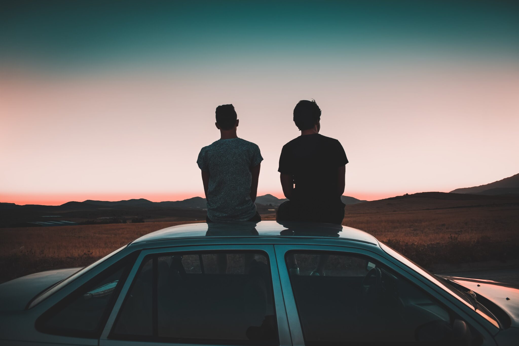 Two men sitting on their car watching sunset
