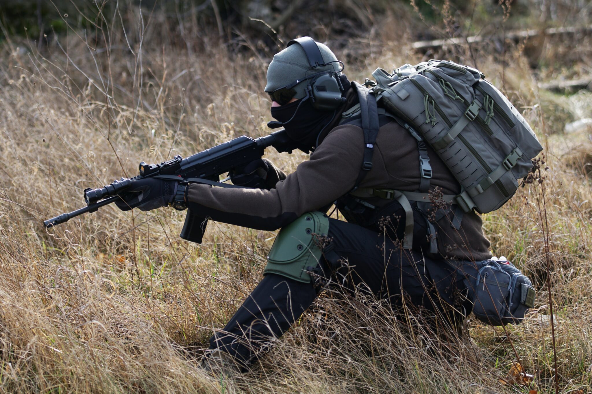 Man with tactical gear and rifle stalking in the grass