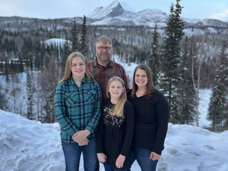 Family photo in the snow with trees and mountains in the background