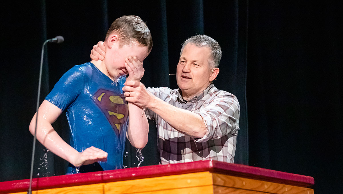 Young boy with superman shirt getting baptized on stage