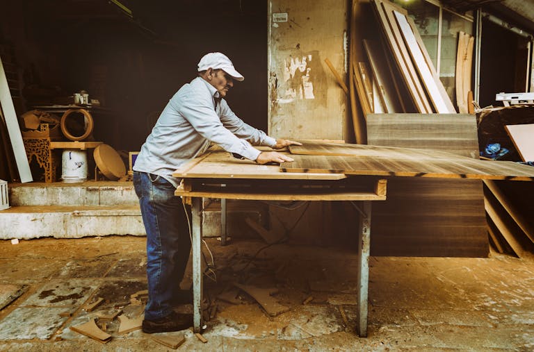 Carpenter focuses on woodworking project inside a busy workshop, surrounded by materials.